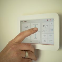 Dłoń obsługująca panel dotykowy sterujący ogrzewaniem w inteligentnym domu.
