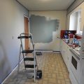Kuchnia w trakcie remontu z drabiną, puszką farby i częściowo pomalowaną ścianą